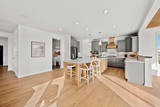 kitchen featuring gray cabinetry, hanging light fixtures, stainless steel refrigerator with ice dispenser, premium range hood, and a breakfast bar area