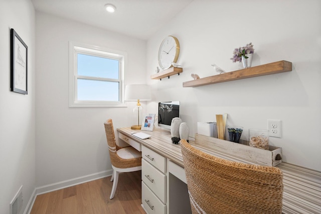 home office with built in desk and light hardwood / wood-style floors