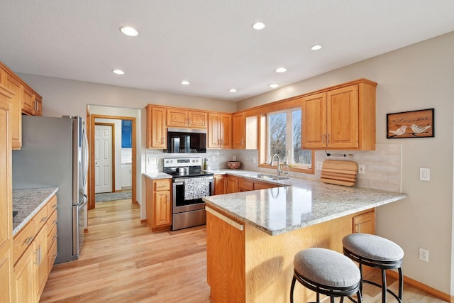 kitchen featuring sink, a breakfast bar area, kitchen peninsula, stainless steel appliances, and light wood-type flooring