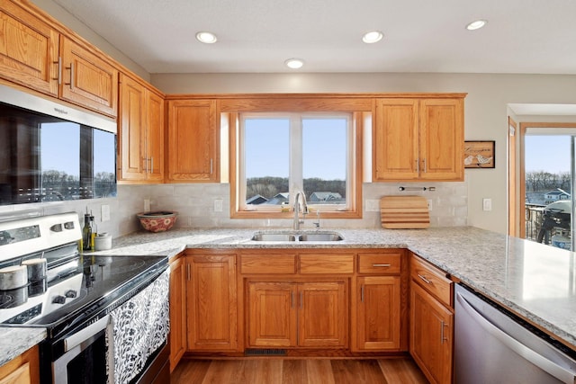 kitchen featuring light stone counters, stainless steel appliances, sink, and light hardwood / wood-style flooring