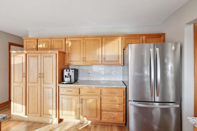 kitchen featuring light stone counters, decorative backsplash, light hardwood / wood-style flooring, and stainless steel refrigerator