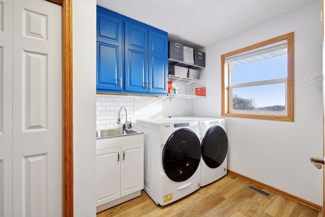 laundry room featuring sink, cabinets, independent washer and dryer, light hardwood / wood-style floors, and a textured ceiling