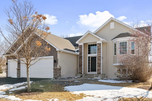 traditional home featuring stone siding, driveway, an attached garage, and a shingled roof