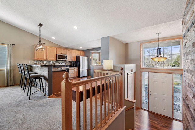 interior space with a peninsula, appliances with stainless steel finishes, dark countertops, decorative light fixtures, and tasteful backsplash