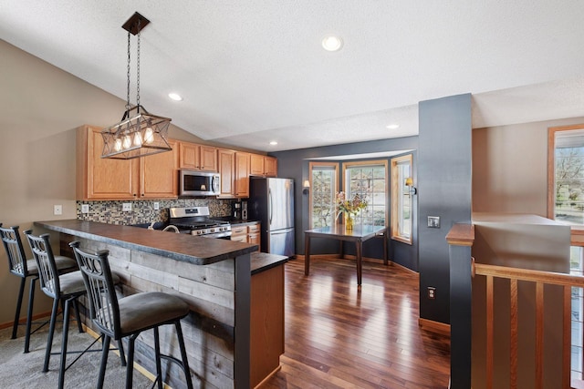 kitchen with a peninsula, lofted ceiling, stainless steel appliances, dark countertops, and backsplash