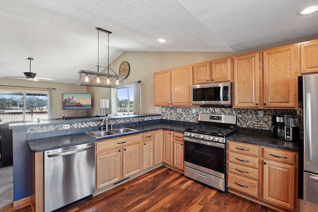 kitchen featuring dark countertops, lofted ceiling, appliances with stainless steel finishes, a peninsula, and a sink