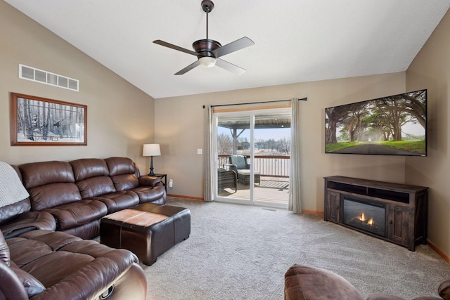 living room featuring visible vents, baseboards, lofted ceiling, carpet flooring, and a glass covered fireplace