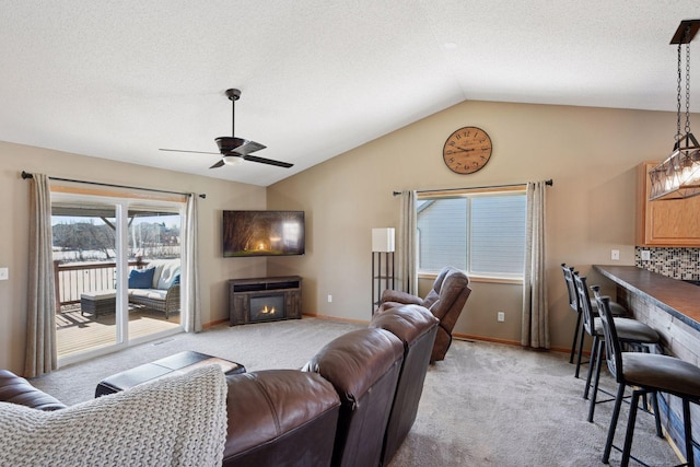 living room with baseboards, light carpet, a glass covered fireplace, and vaulted ceiling