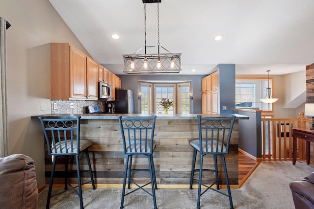 kitchen featuring carpet floors, decorative backsplash, a peninsula, a kitchen breakfast bar, and stainless steel appliances