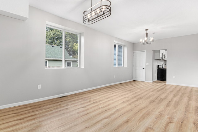 unfurnished living room with sink, light wood-type flooring, and an inviting chandelier