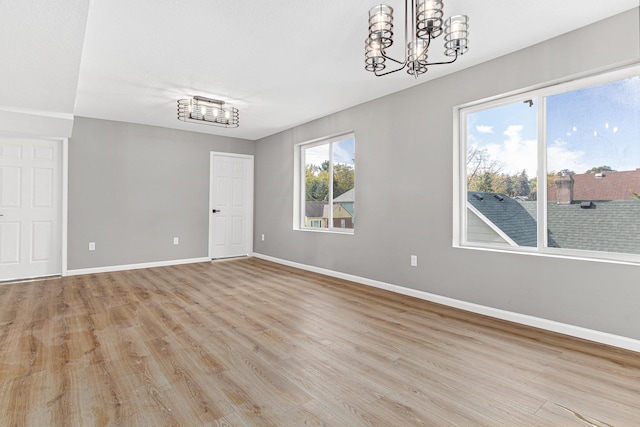 empty room featuring a wealth of natural light, light hardwood / wood-style flooring, and a chandelier