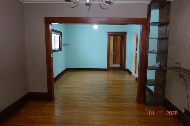 spare room with wood-type flooring, ornamental molding, and a notable chandelier