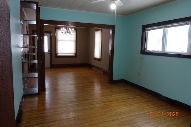 spare room with ceiling fan with notable chandelier, a wealth of natural light, wood-type flooring, and ornamental molding