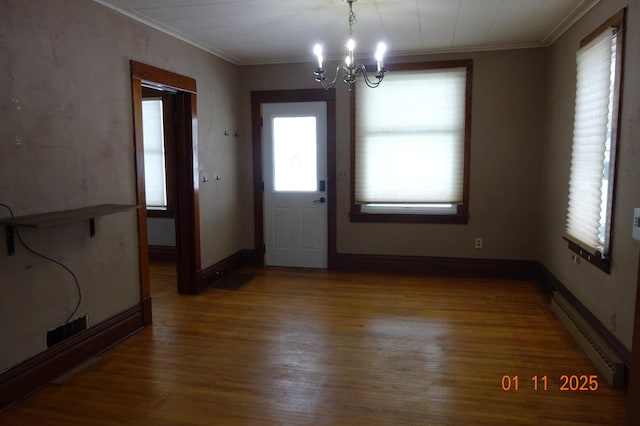 unfurnished dining area featuring a baseboard radiator, a wealth of natural light, wood-type flooring, an inviting chandelier, and crown molding