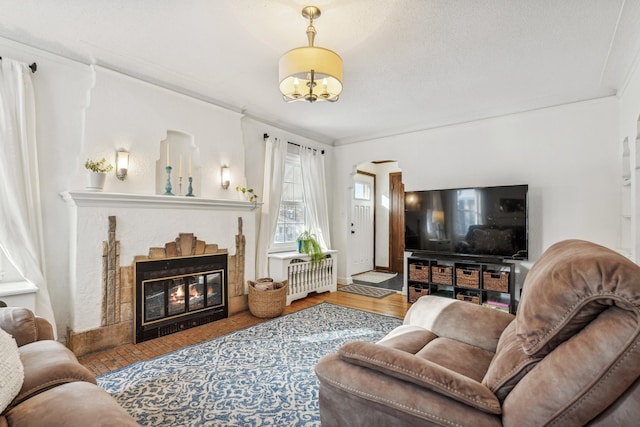 living room with a tile fireplace, a textured ceiling, wood-type flooring, radiator heating unit, and crown molding