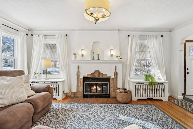 living area with a tile fireplace, hardwood / wood-style flooring, crown molding, and radiator heating unit