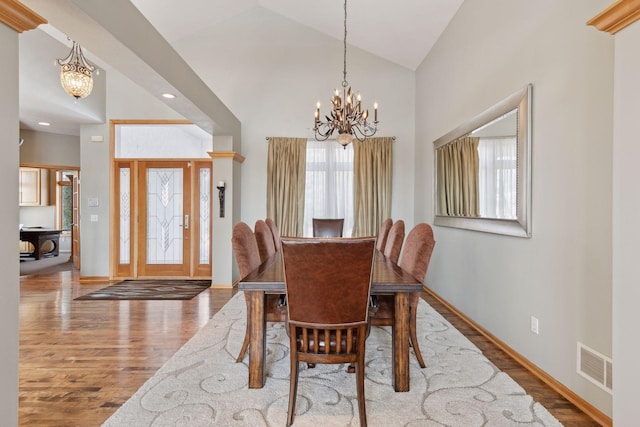 dining area featuring an inviting chandelier, wood-type flooring, and high vaulted ceiling