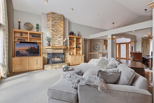 living room with a notable chandelier, a stone fireplace, vaulted ceiling, and french doors