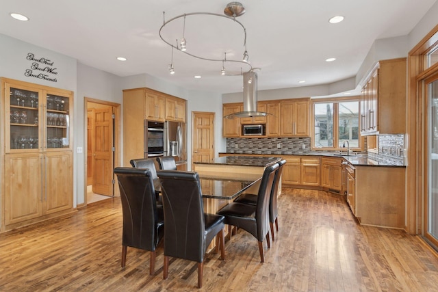 kitchen featuring tasteful backsplash, sink, island exhaust hood, stainless steel appliances, and light hardwood / wood-style flooring