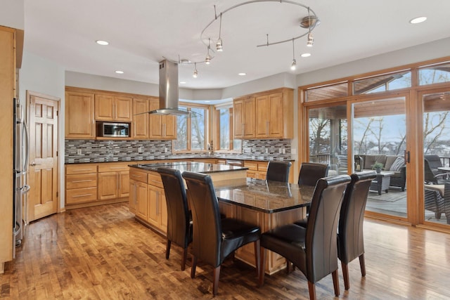 kitchen with a breakfast bar, a center island, stainless steel microwave, island range hood, and light wood-type flooring