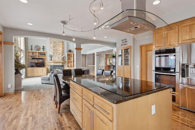 kitchen with light brown cabinetry, island range hood, appliances with stainless steel finishes, a kitchen island, and a fireplace