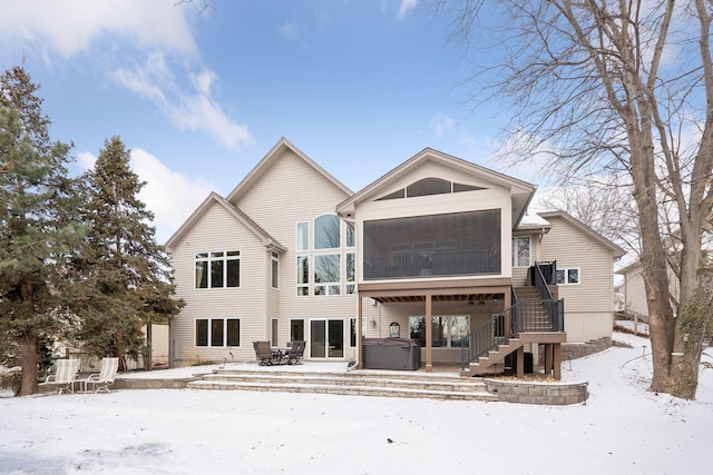 snow covered rear of property featuring a hot tub and a sunroom