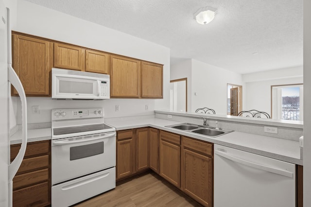 kitchen with kitchen peninsula, a textured ceiling, white appliances, sink, and light hardwood / wood-style flooring