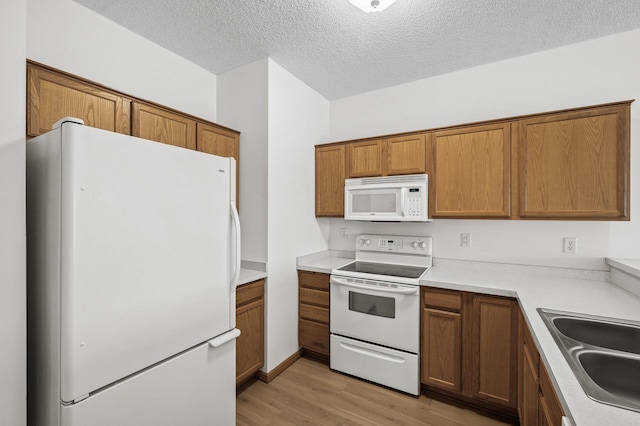 kitchen featuring a textured ceiling, white appliances, light hardwood / wood-style floors, and sink