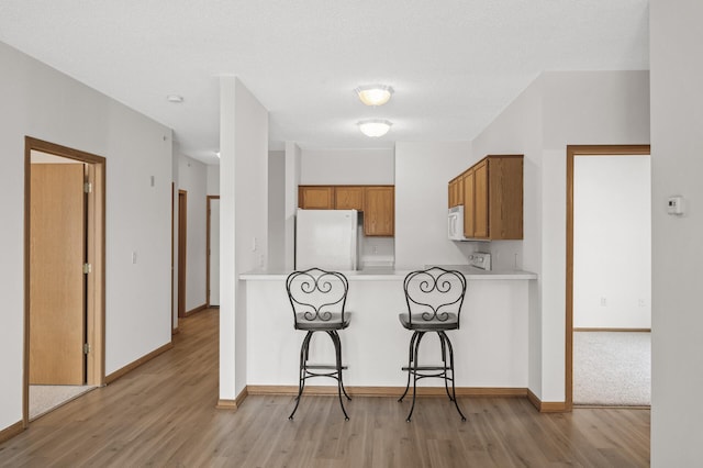 kitchen featuring white appliances, light hardwood / wood-style flooring, a textured ceiling, a kitchen bar, and kitchen peninsula