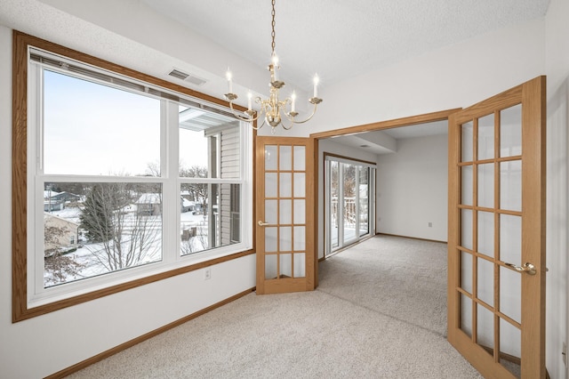 carpeted empty room featuring an inviting chandelier, a textured ceiling, and french doors