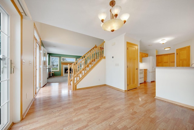 foyer entrance featuring baseboards, light wood finished floors, a notable chandelier, and stairway