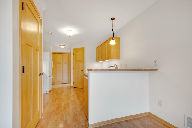kitchen with freestanding refrigerator, light wood-type flooring, a peninsula, a sink, and baseboards