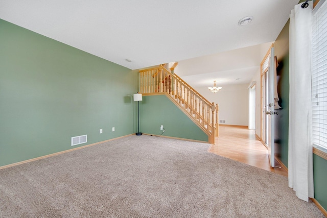 empty room with baseboards, a chandelier, stairway, carpet floors, and visible vents