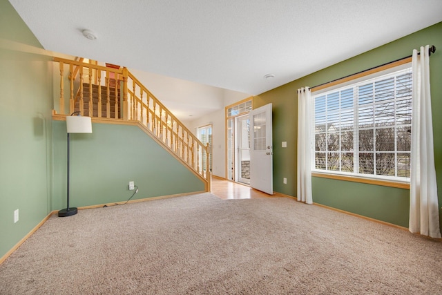 unfurnished living room with stairs, plenty of natural light, baseboards, and carpet floors