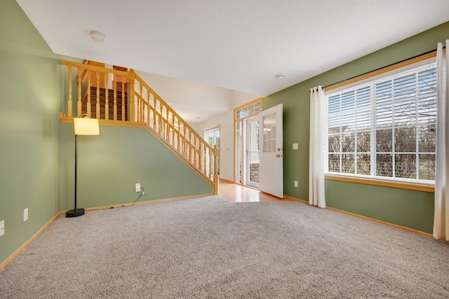 unfurnished living room with baseboards, stairway, and carpet flooring