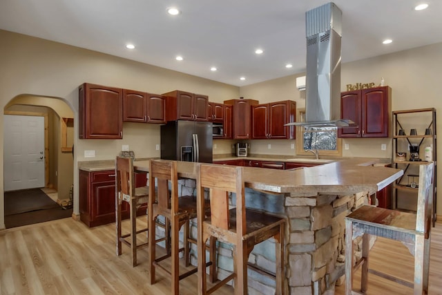 kitchen with island range hood, stainless steel appliances, a peninsula, a kitchen breakfast bar, and light wood-type flooring