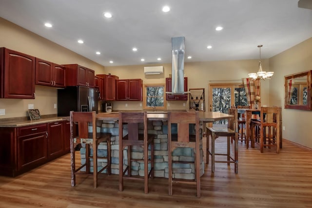 kitchen featuring reddish brown cabinets, light wood-style flooring, a breakfast bar area, a wall mounted air conditioner, and decorative light fixtures