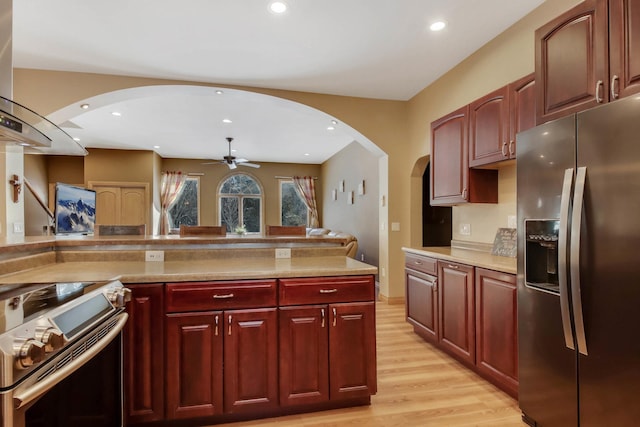 kitchen featuring arched walkways, a ceiling fan, dark brown cabinets, appliances with stainless steel finishes, and ventilation hood