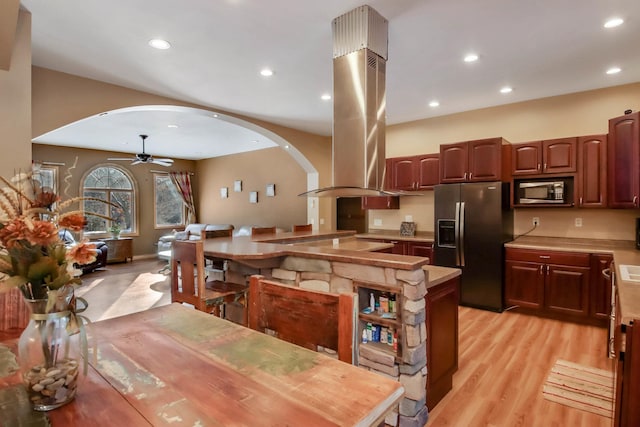 kitchen with light countertops, ceiling fan, arched walkways, island range hood, and stainless steel fridge with ice dispenser