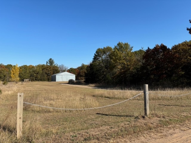view of yard featuring a detached garage, a rural view, and an outbuilding