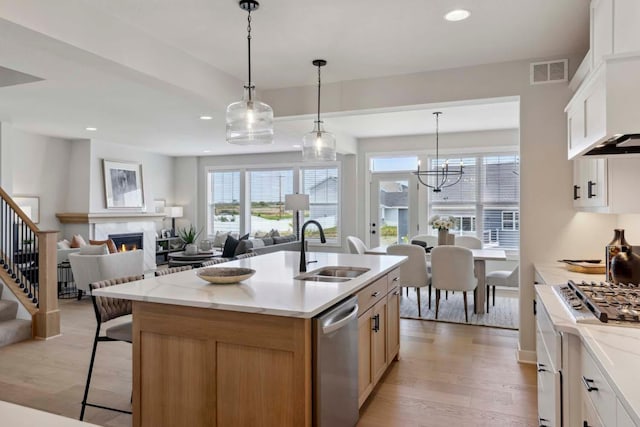 kitchen featuring dishwasher, a kitchen island with sink, white cabinets, sink, and light stone counters