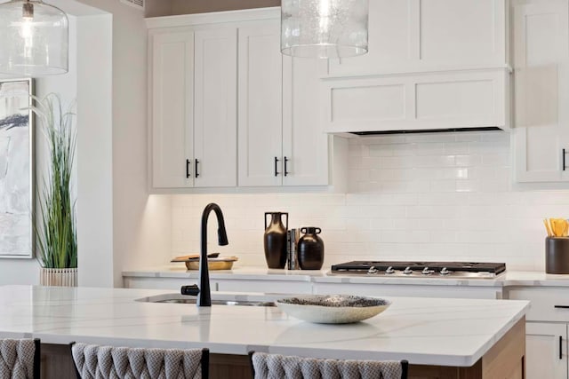 kitchen featuring light stone countertops, tasteful backsplash, white cabinetry, and hanging light fixtures