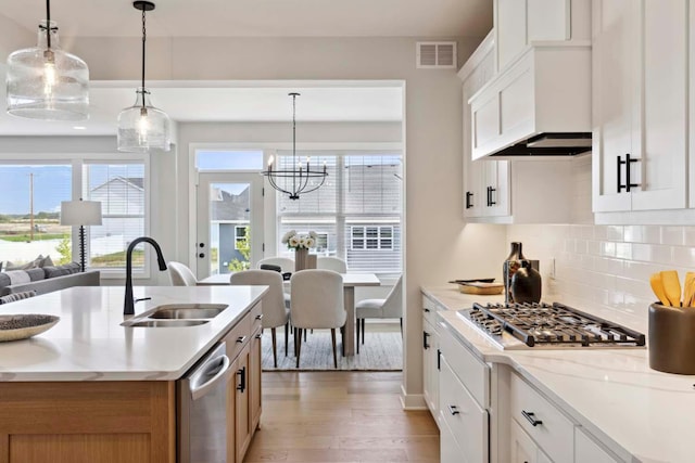 kitchen with light stone countertops, appliances with stainless steel finishes, sink, pendant lighting, and white cabinetry