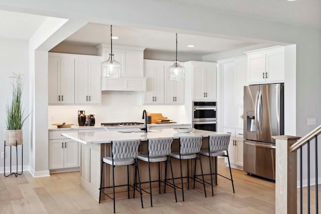 kitchen featuring white cabinetry, decorative light fixtures, a kitchen island with sink, appliances with stainless steel finishes, and light wood-type flooring