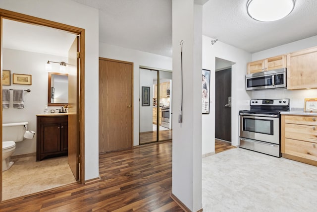 kitchen with a textured ceiling, light brown cabinetry, stainless steel appliances, and dark hardwood / wood-style floors