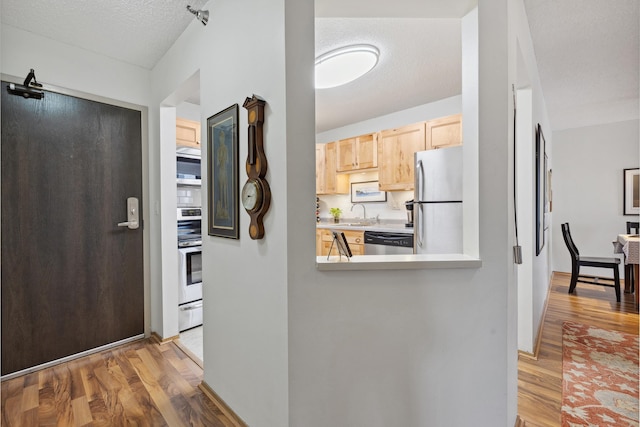 interior space with hardwood / wood-style floors, light brown cabinetry, stainless steel appliances, and a textured ceiling