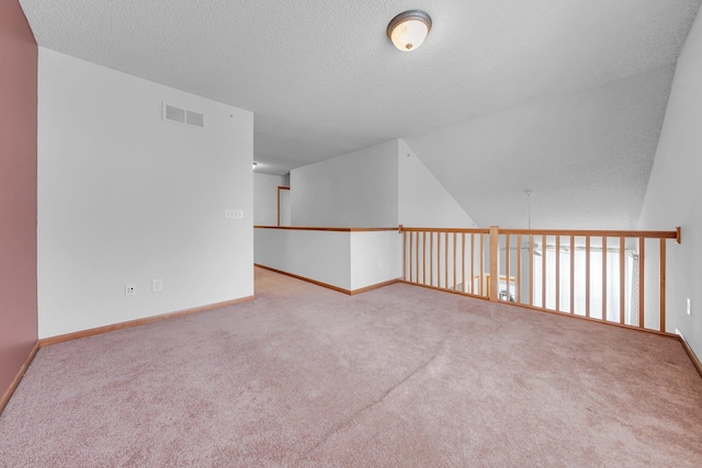 spare room featuring lofted ceiling, a textured ceiling, and light carpet