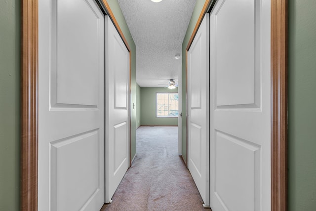 hallway featuring light colored carpet and a textured ceiling