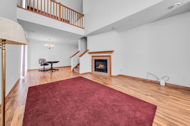 unfurnished living room featuring a towering ceiling, a tile fireplace, a chandelier, and hardwood / wood-style floors