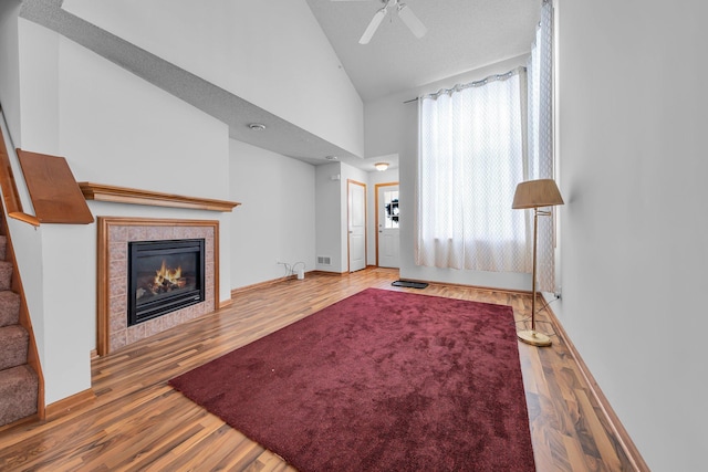 living room featuring wood-type flooring, a tiled fireplace, high vaulted ceiling, and ceiling fan